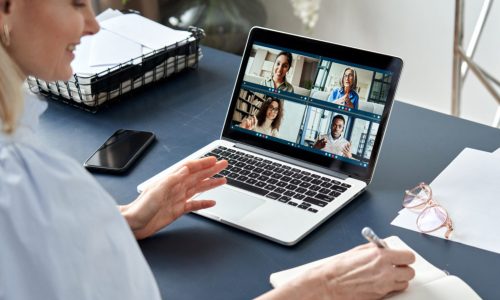 Business woman having virtual team meeting on video conference call using laptop computer. Social distance work from home office with diverse people group in remote online chat. Over shoulder view